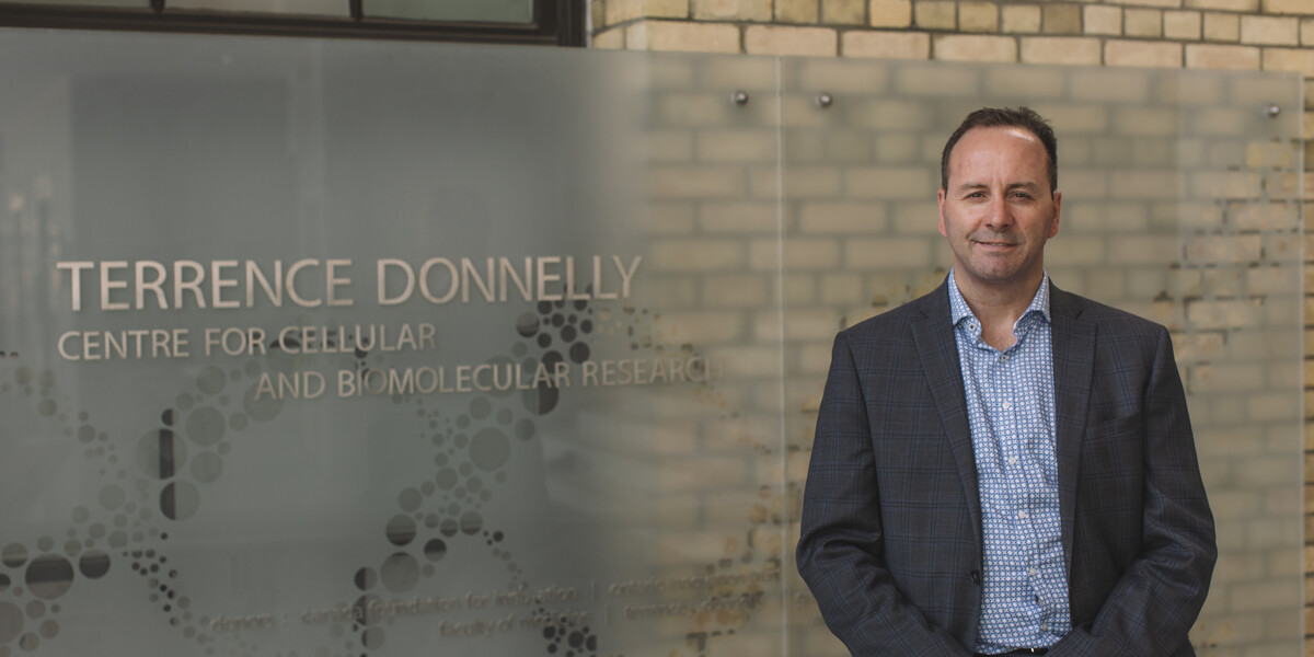 director Angers standing beside Donnelly Centre sign