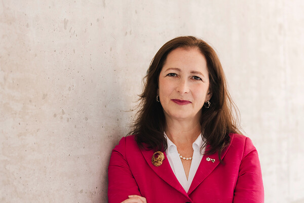 white woman with shoulder length hair wearing a fushia blaser leaning against wall