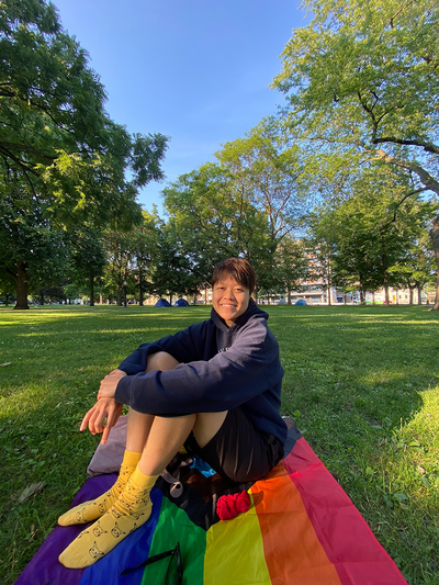 A young female sitting on a pride blanket in park
