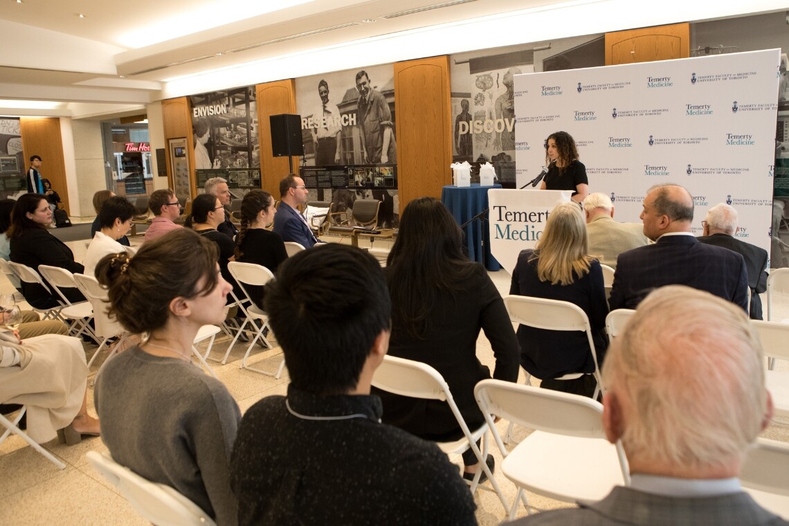 Woman speaking to audience in front of Temerty Faculty of Medicine branded backdrop