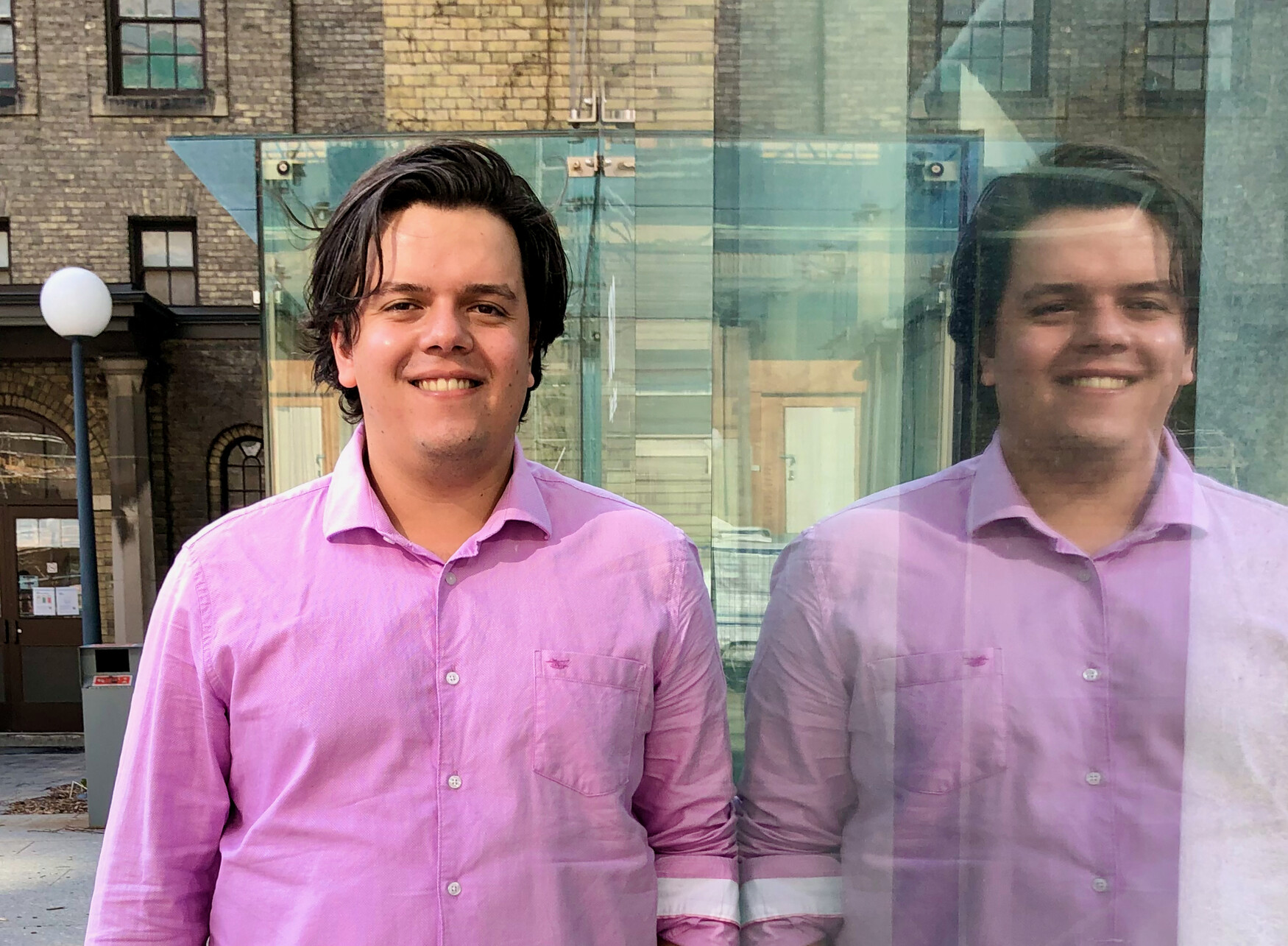 white male in pink shirt leaning against a glass wall with his mirror image reflection