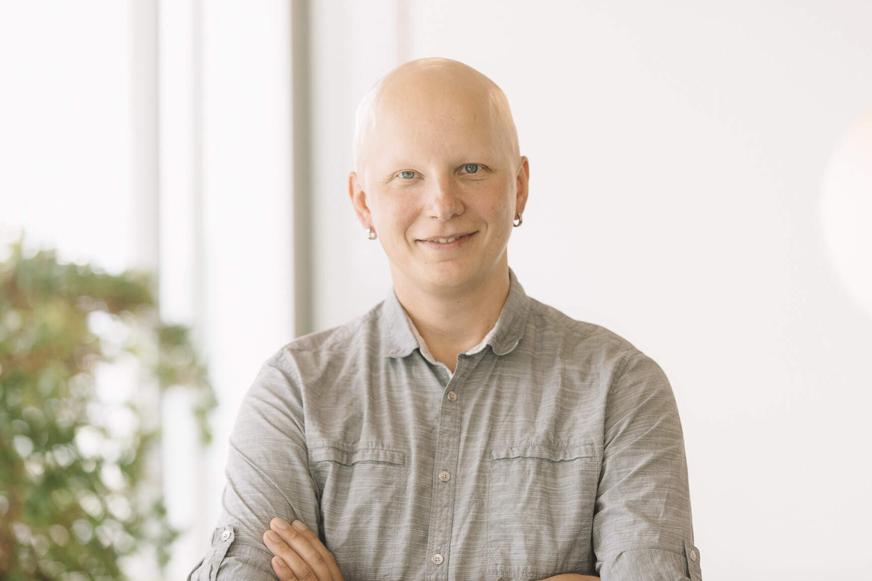 white bald male in grey shirt with greenery in background